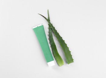 Tube of toothpaste and fresh aloe on white background, top view