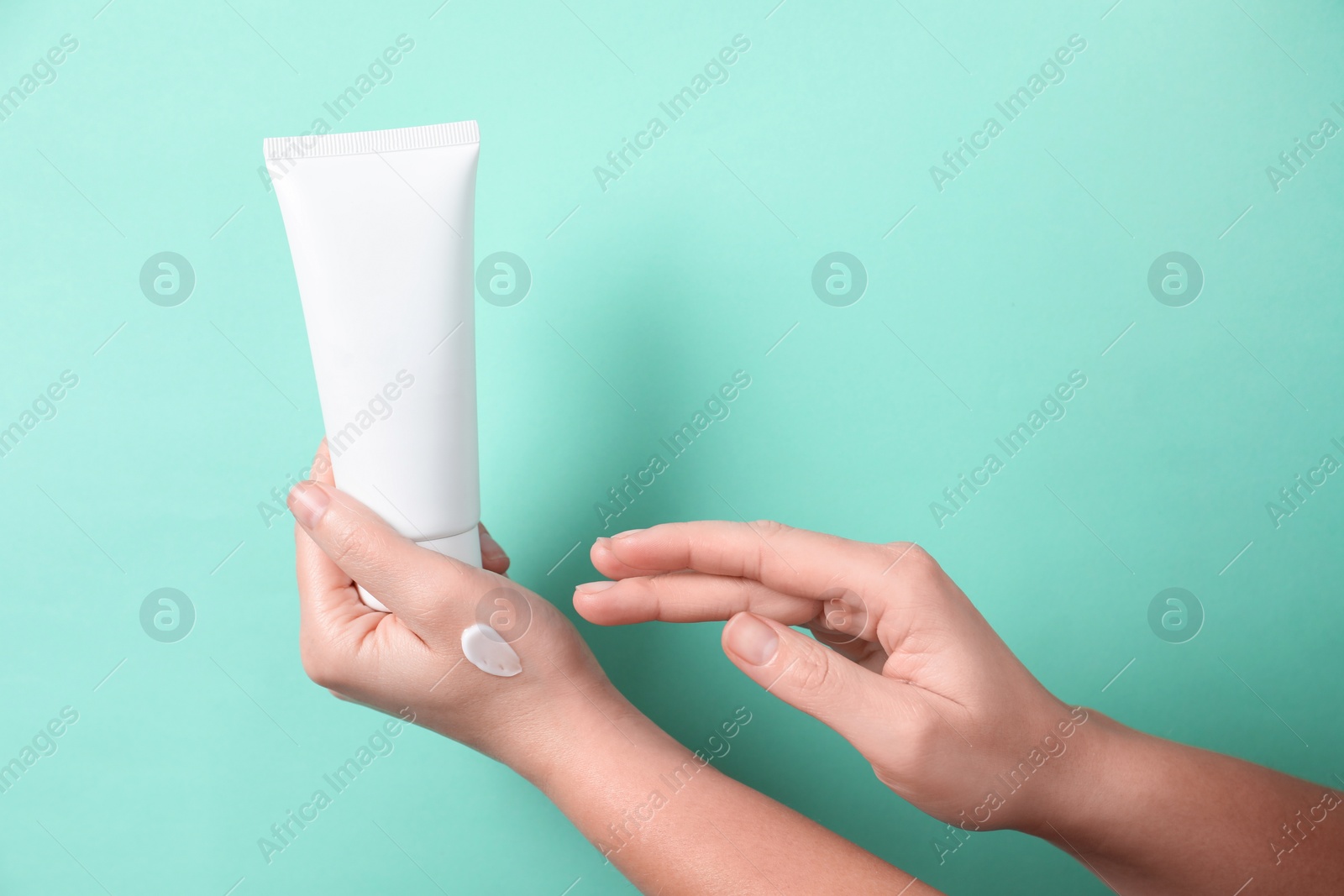 Photo of Woman with tube applying cosmetic cream onto her hand on turquoise background, closeup