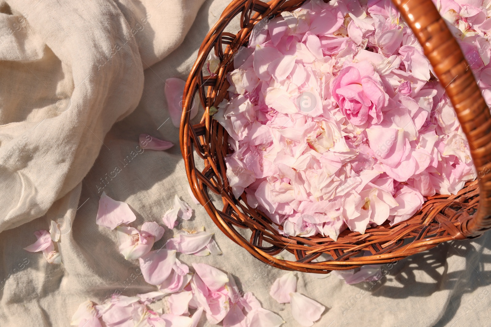 Photo of Wicker basket of beautiful tea rose petals on beige fabric, flat lay