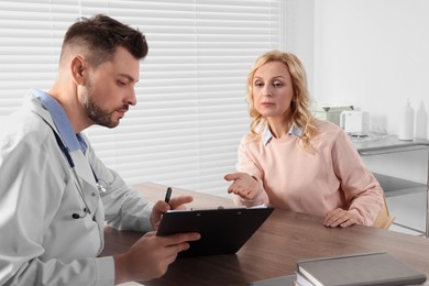 Photo of Doctor with clipboard consulting patient at table in clinic