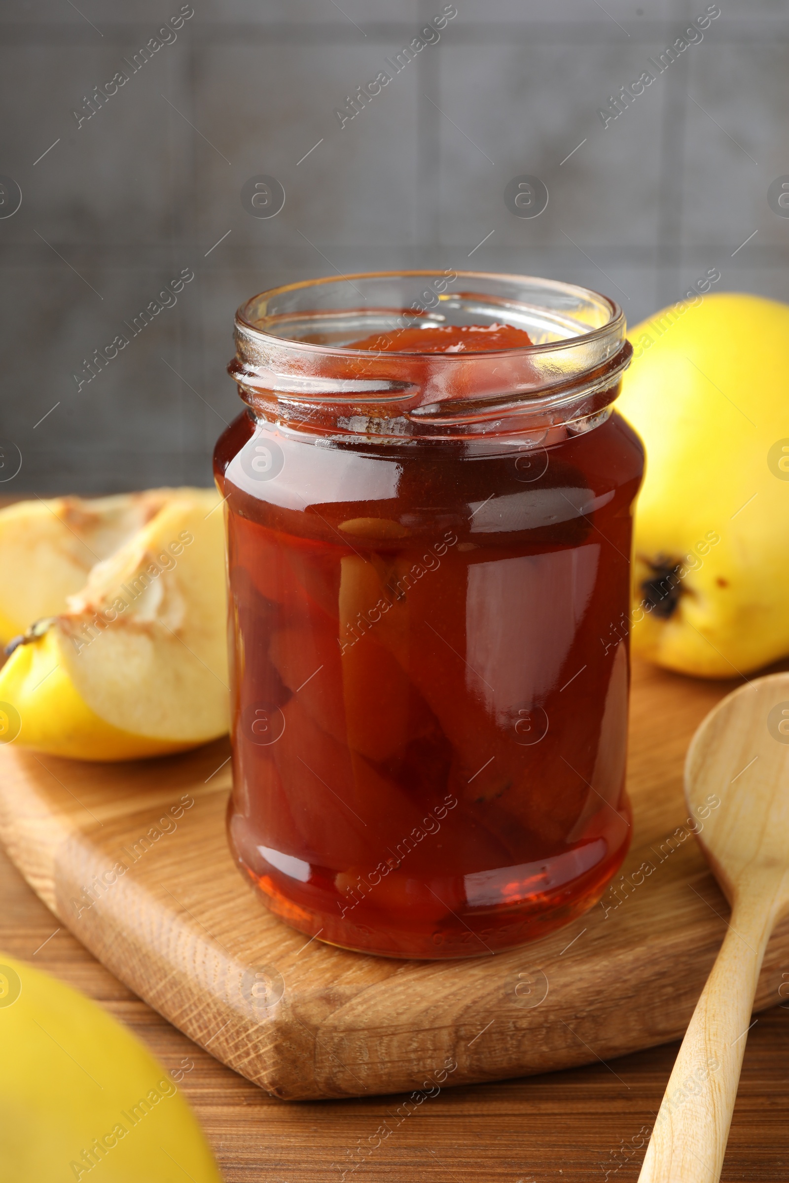 Photo of Tasty homemade quince jam in jar and fruits on wooden table