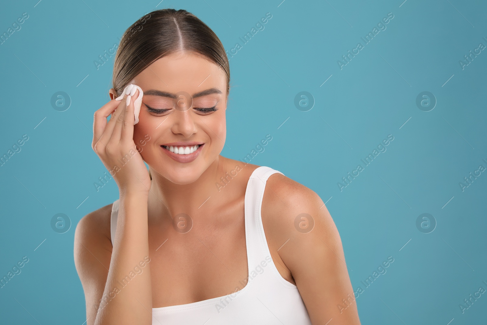 Photo of Beautiful woman removing makeup with cotton pad on light blue background. Space for text