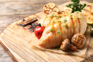 Wooden board with grilled chicken breasts and garnish on table, closeup