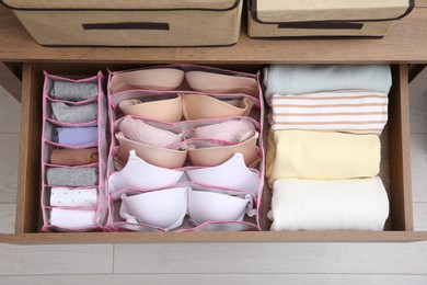 Photo of Open drawer with folded clothes and underwear indoors, top view. Vertical storage