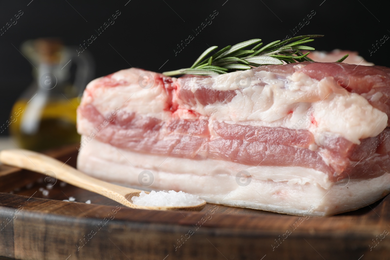 Photo of Piece of raw pork belly, salt and rosemary on wooden board, closeup