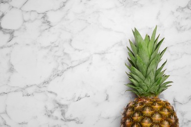 Photo of Whole ripe pineapple on white marble table, top view. Space for text
