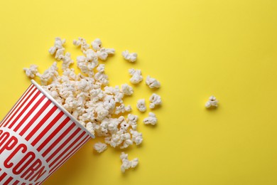 Photo of Overturned paper cup with delicious popcorn on yellow background, flat lay. Space for text