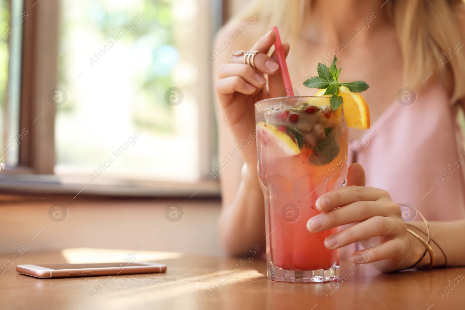 Photo of Young woman with glass of tasty natural lemonade in cafe, closeup. Detox drink