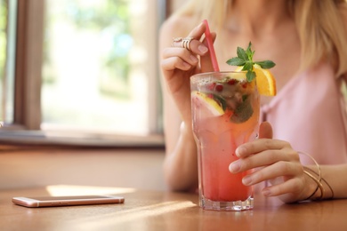 Young woman with glass of tasty natural lemonade in cafe, closeup. Detox drink