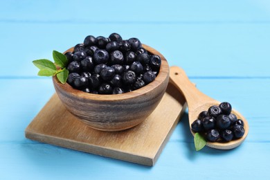 Ripe bilberries and leaves on light blue wooden table, closeup