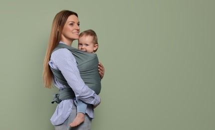 Mother holding her child in baby wrap on olive background. Space for text