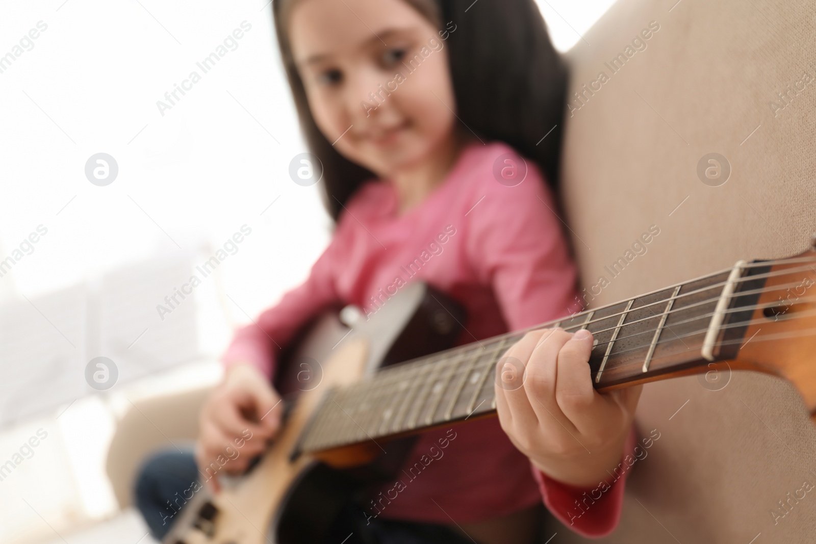 Photo of Little girl playing guitar at home, closeup. Learning music notes