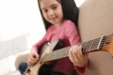 Photo of Little girl playing guitar at home, closeup. Learning music notes