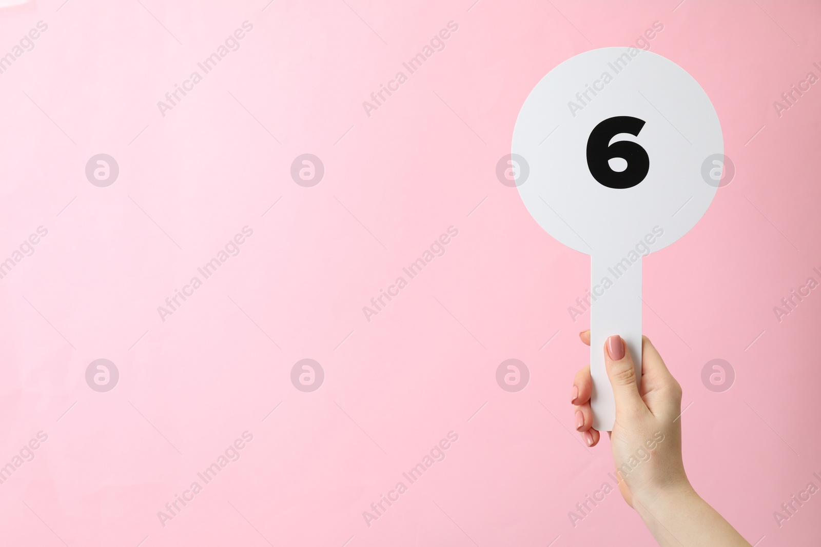 Photo of Woman holding auction paddle with number 6 on pink background, closeup. Space for text