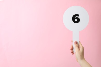 Woman holding auction paddle with number 6 on pink background, closeup. Space for text