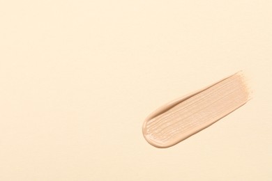 Photo of Smear of skin foundation on beige background, top view. Space for text