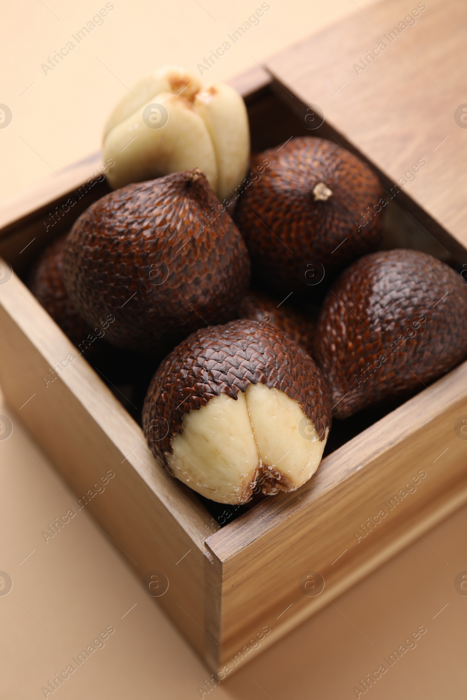 Photo of Wooden crate with fresh salak fruits on beige background, closeup