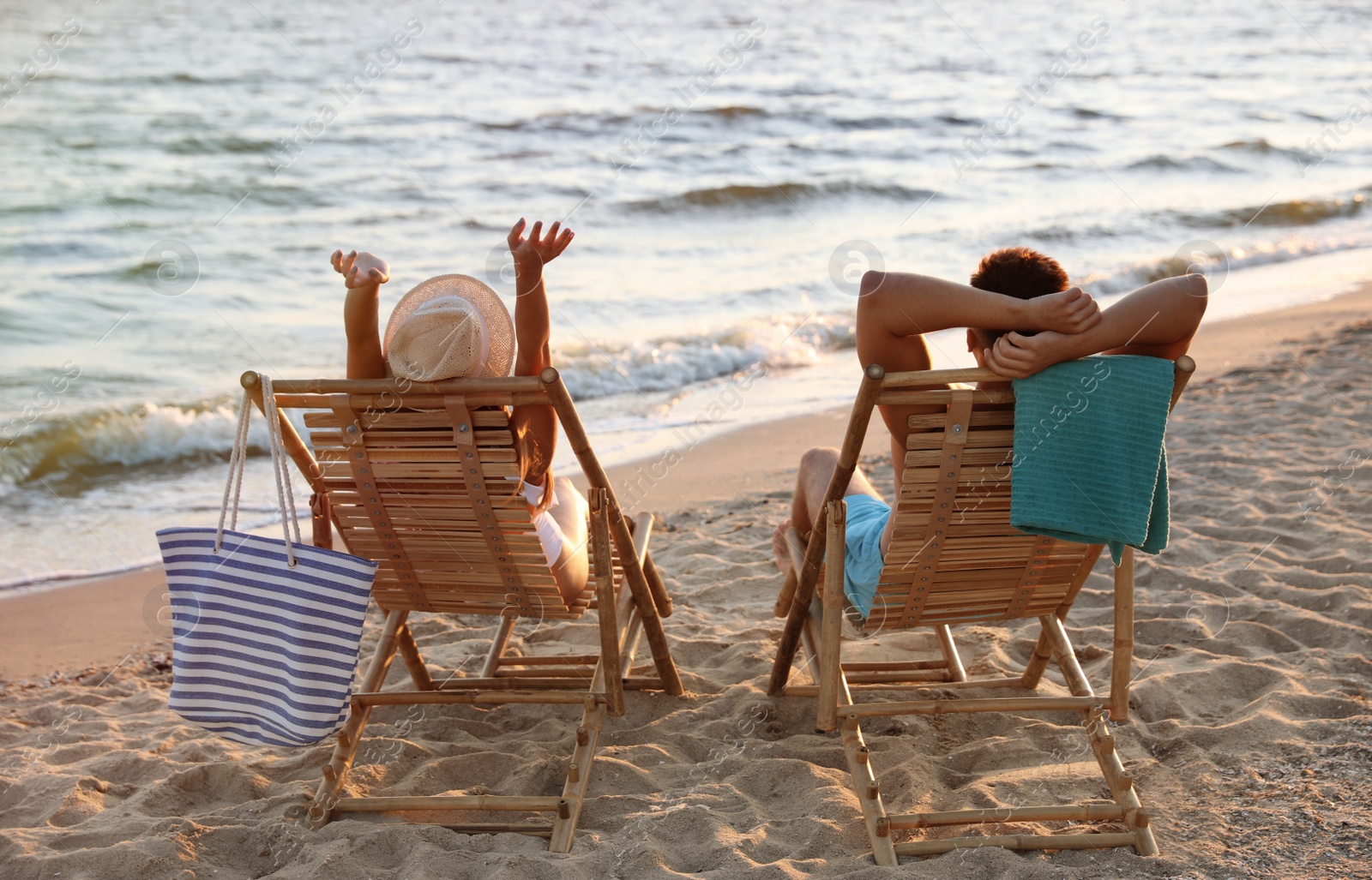 Photo of Young couple relaxing in deck chairs on beach near sea