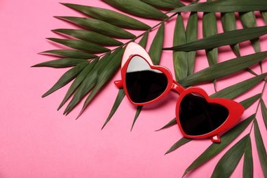 Photo of Stylish heart shaped glasses with tropical leaves on color background. Space for text