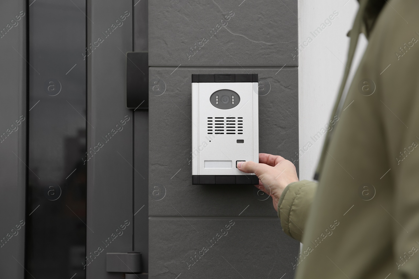 Photo of Man ringing intercom with camera near building entrance, closeup