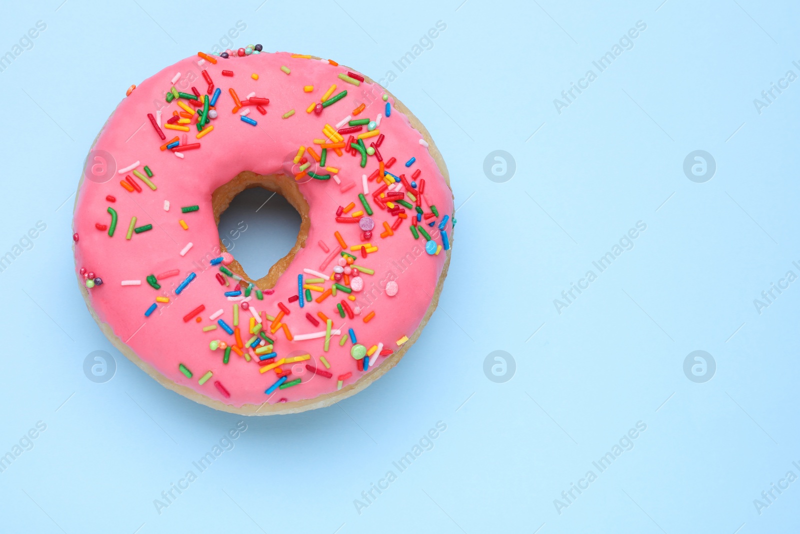 Photo of Glazed donut decorated with sprinkles on light blue background, top view. Space for text. Tasty confectionery