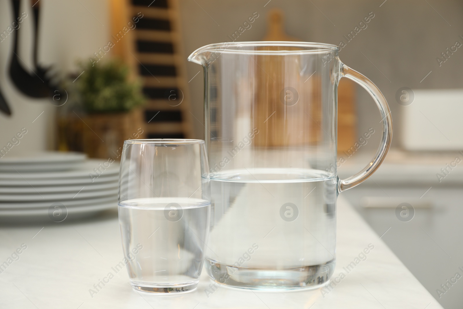 Photo of Jug and glass with clear water on white table in kitchen