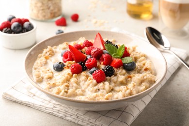Photo of Bowl of oatmeal porridge served with berries on light grey table, closeup
