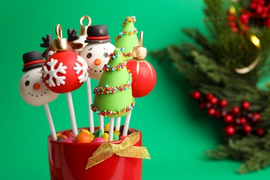 Photo of Delicious Christmas themed cake pops on green background, closeup. Space for text