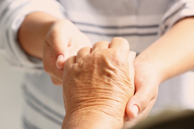 Photo of Helping hands holding together, closeup. Elderly care concept