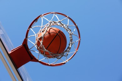 Basketball ball and hoop with net outdoors on sunny day, bottom view