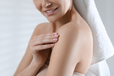 Woman applying body oil onto shoulder on light grey background, closeup