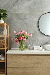 Photo of Vase with beautiful pink tulips and toiletries near sink in bathroom