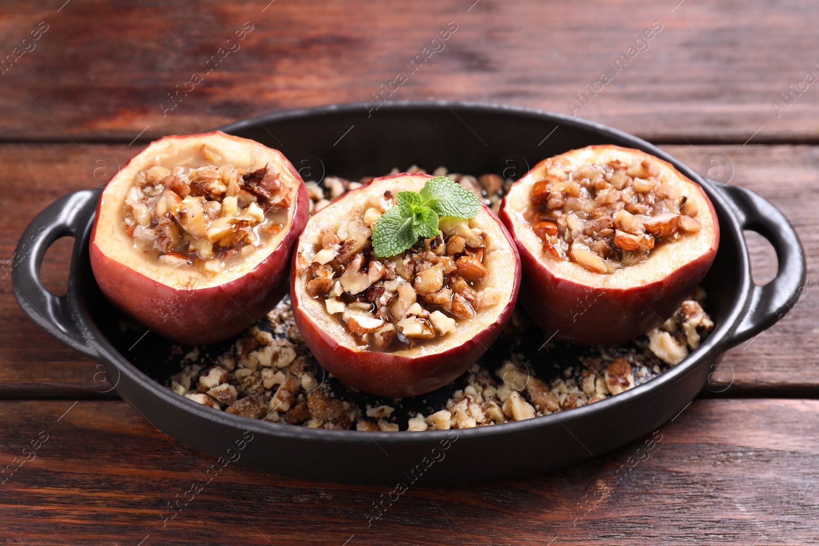 Photo of Tasty baked apples with nuts, honey and mint in baking dish on wooden table, closeup