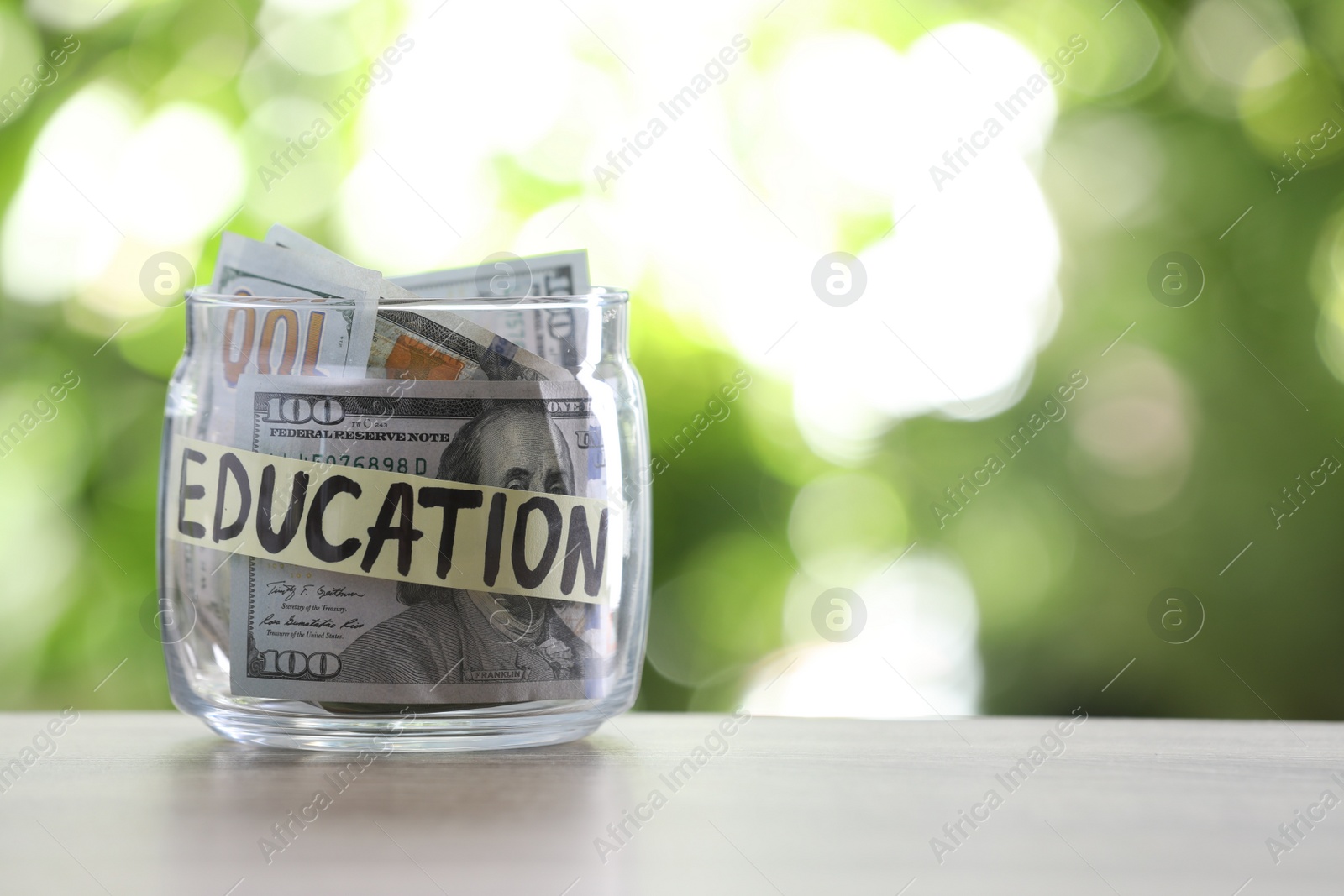 Photo of Glass jar with money and label EDUCATION on table against blurred background. Space for text