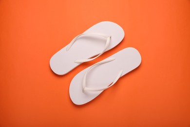 Photo of Stylish white flip flops on orange background, top view