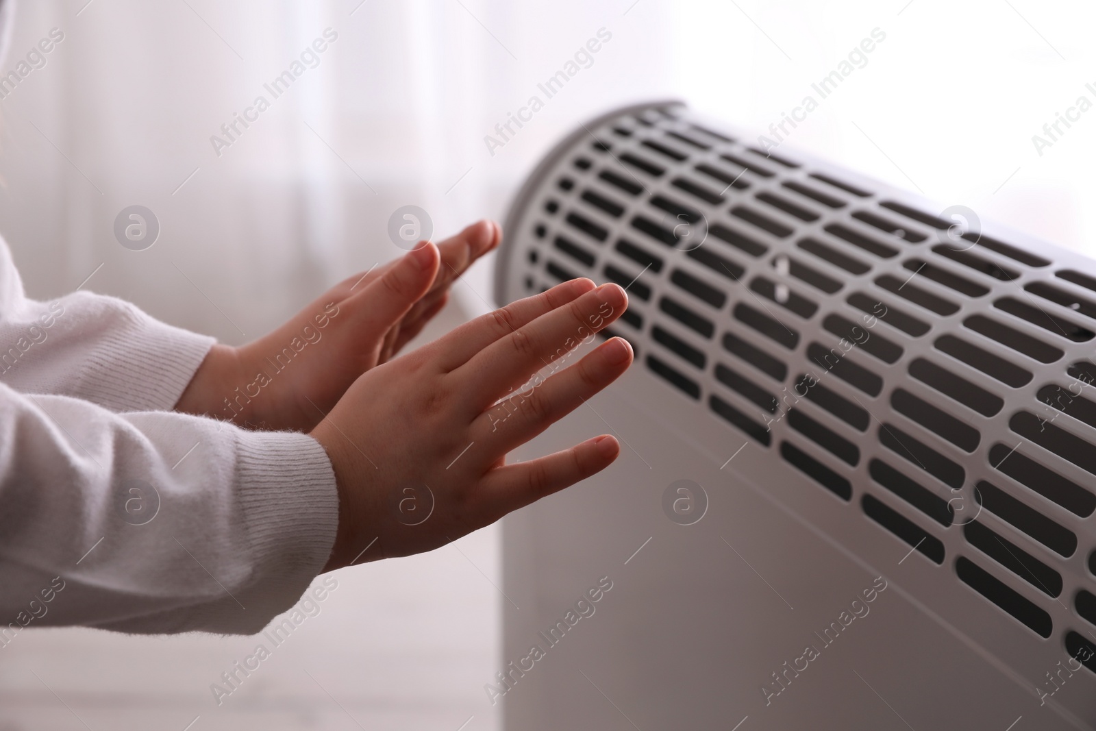 Photo of Child warming hands near electric heater at home, closeup