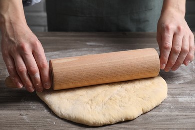 Photo of Woman rolling raw dough at wooden table, closeup