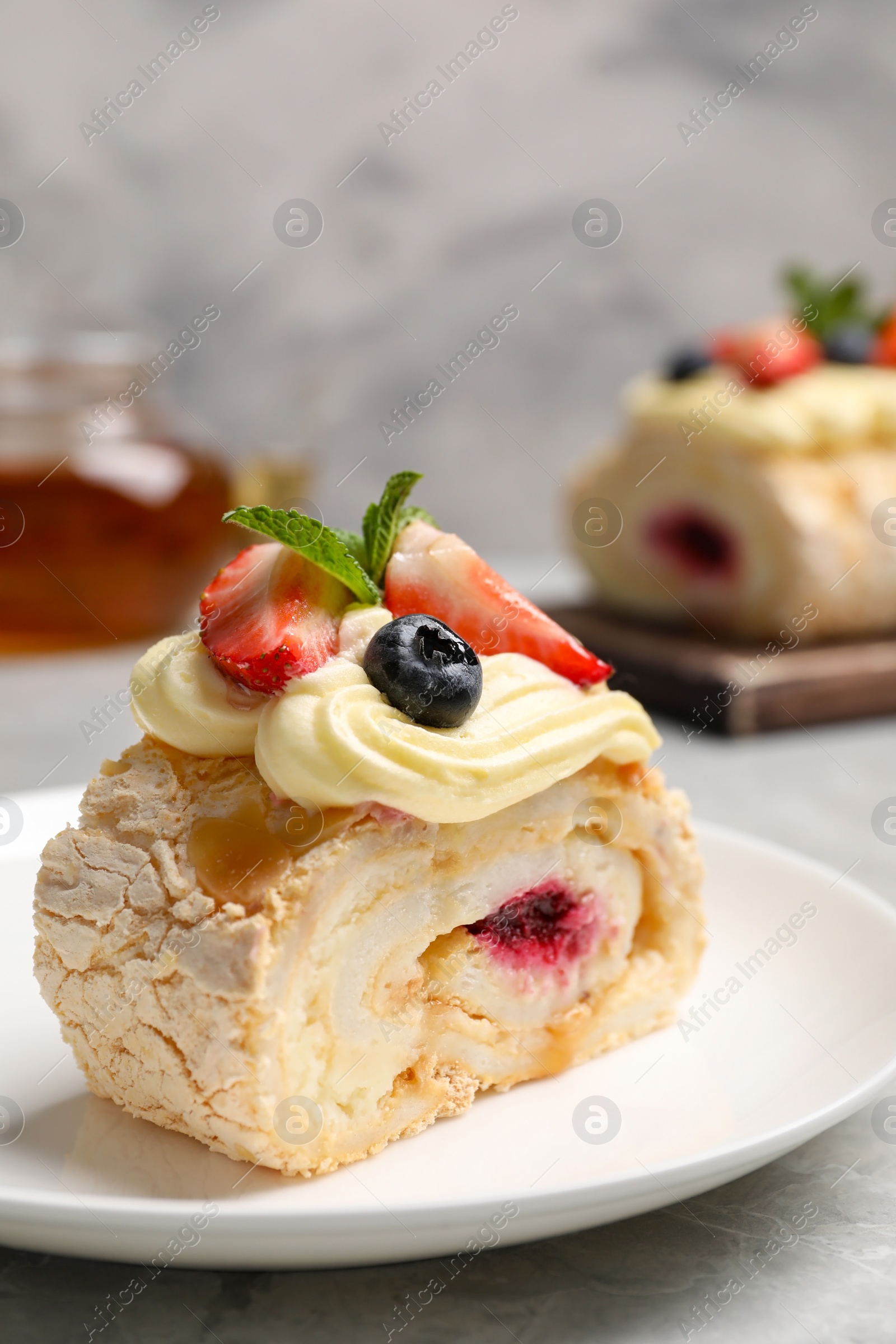 Photo of Piece of tasty meringue roll with jam, cream, strawberry, blueberry and mint on light grey table, closeup