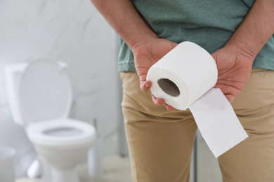 Photo of Man with toilet paper suffering from hemorrhoid in rest room, closeup