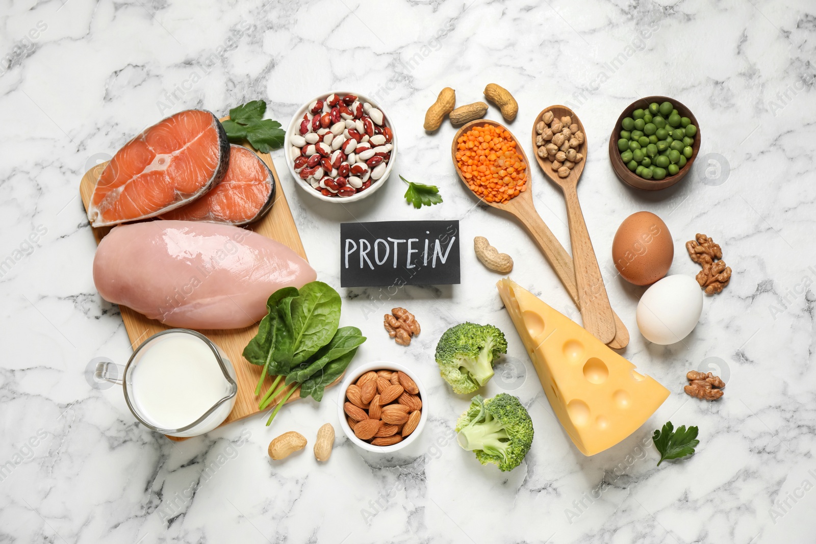 Photo of Card with word PROTEIN and different products on white marble table, flat lay