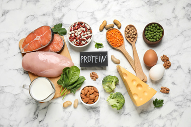 Card with word PROTEIN and different products on white marble table, flat lay