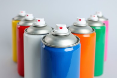 Photo of Colorful cans of spray paints on light grey background, closeup