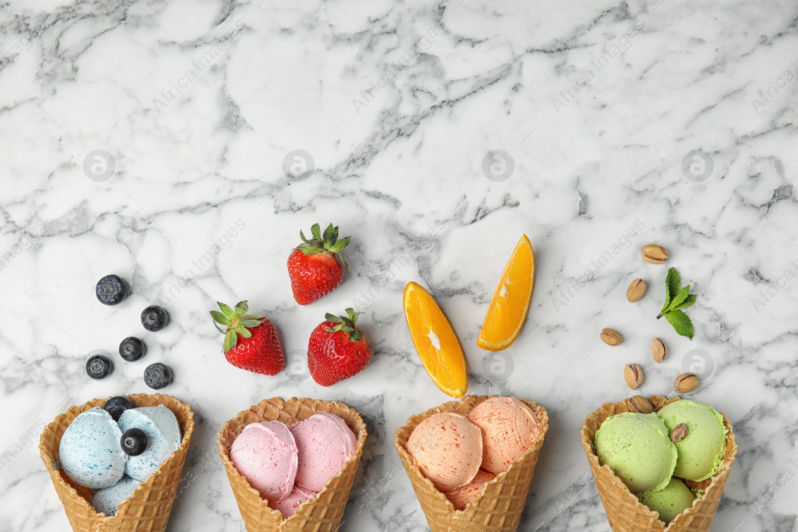 Photo of Flat lay composition with delicious ice creams in waffle cones on marble table, space for text