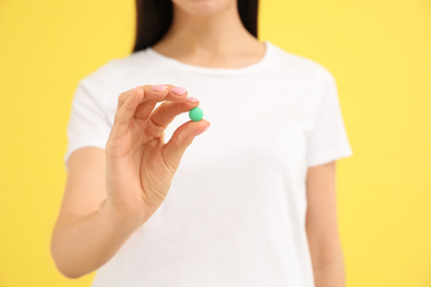 Young woman with vitamin pill on yellow background, closeup