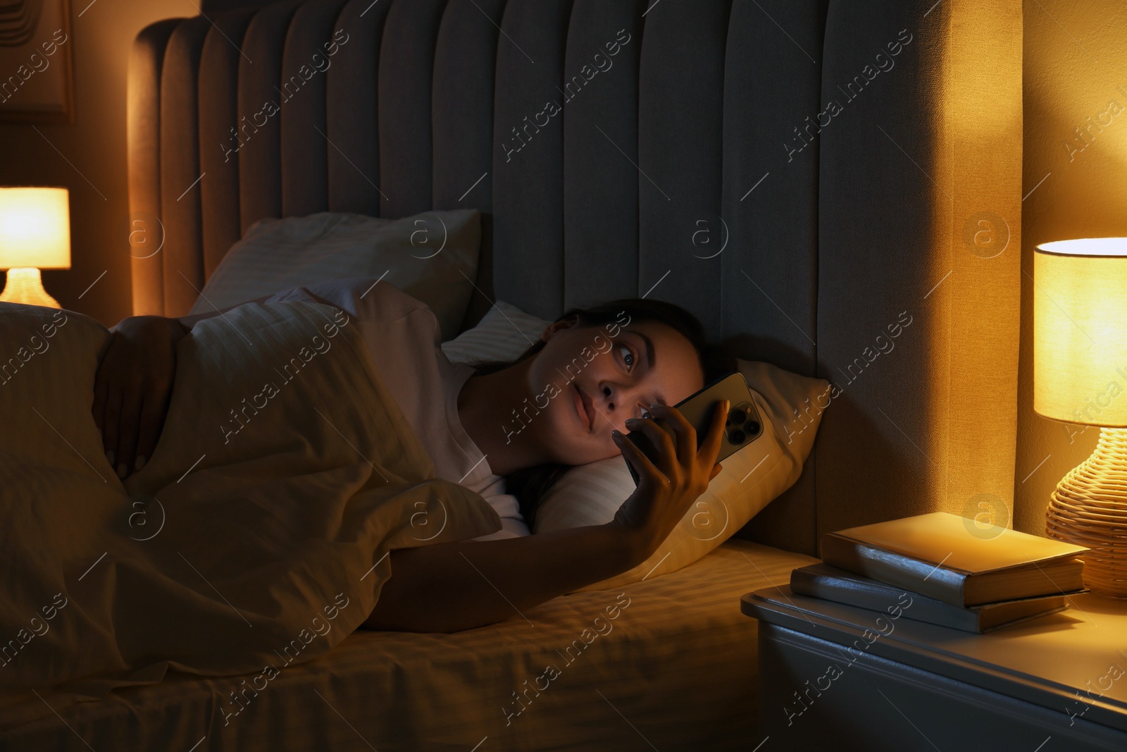 Photo of Woman using smartphone in bed at night. Internet addiction