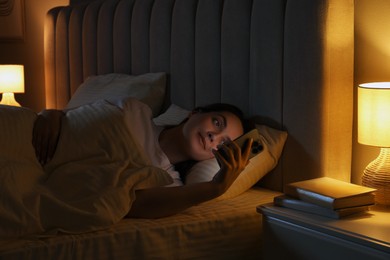 Photo of Woman using smartphone in bed at night. Internet addiction