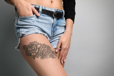 Photo of Beautiful woman with tattoos on leg against grey background, closeup. Space for text
