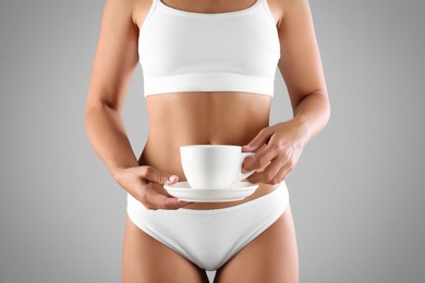 Photo of Young woman holding cup of diet tea on grey background, closeup