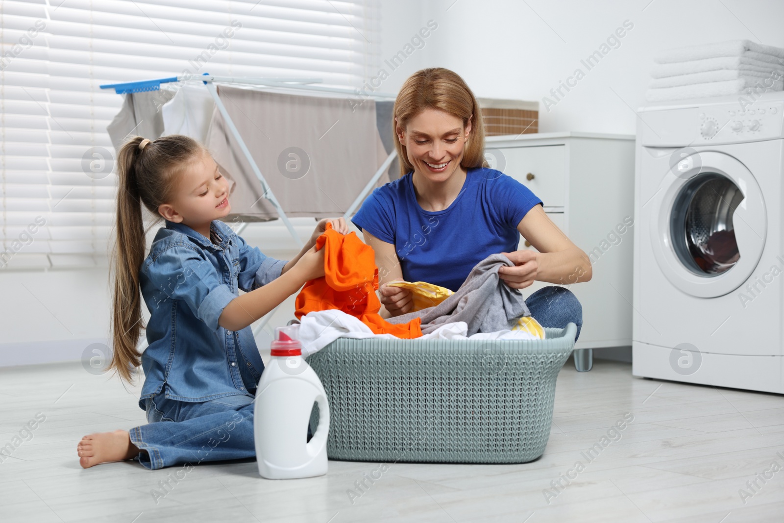 Photo of Mother and daughter taking out dirty clothes from basket in bathroom, space for text