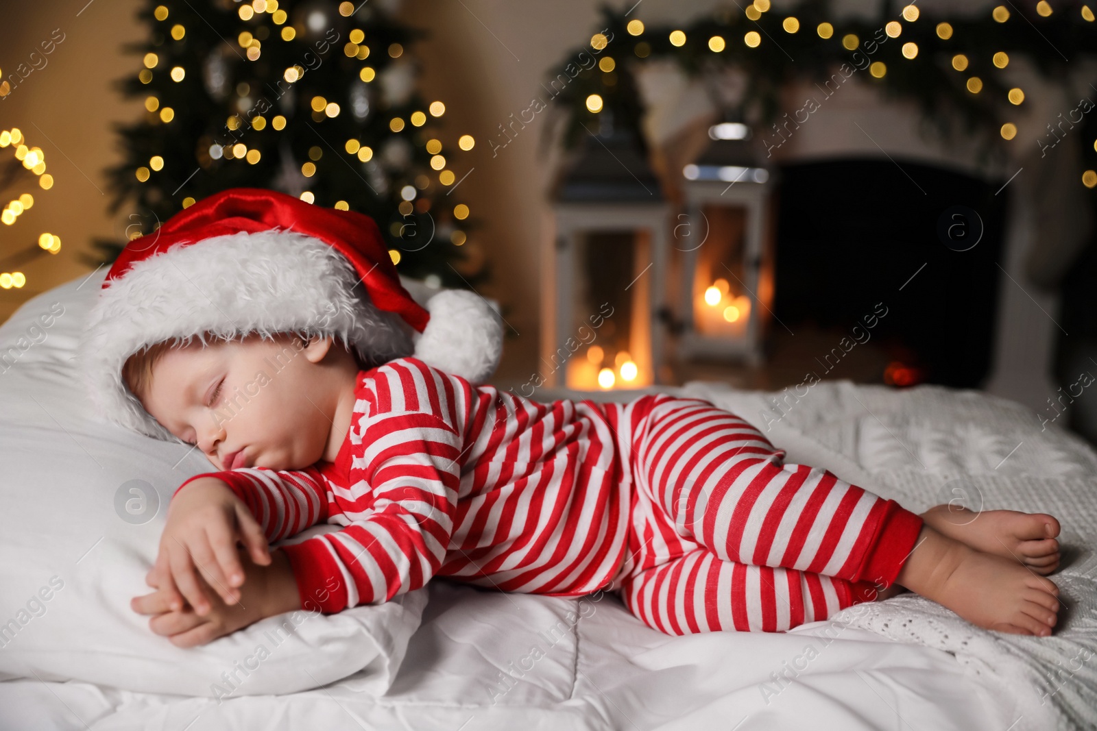 Photo of Baby in Christmas pajamas and Santa hat sleeping on bed indoors